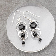 Silver handmade earrings with black tourmaline stone beads on a gray stone surface