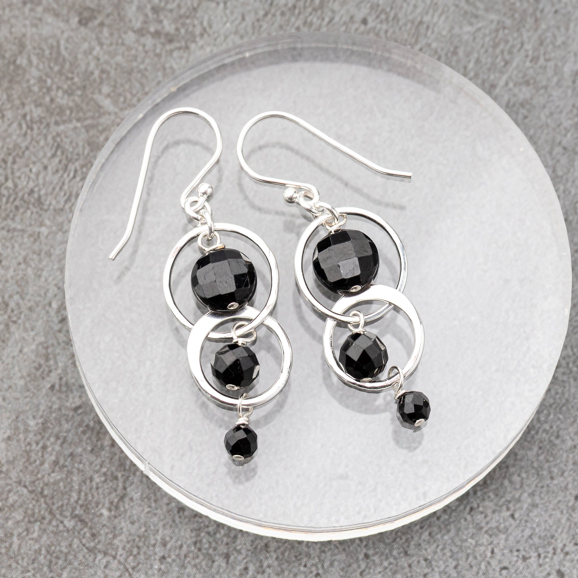 Silver handmade earrings with black tourmaline stone beads on a gray stone surface