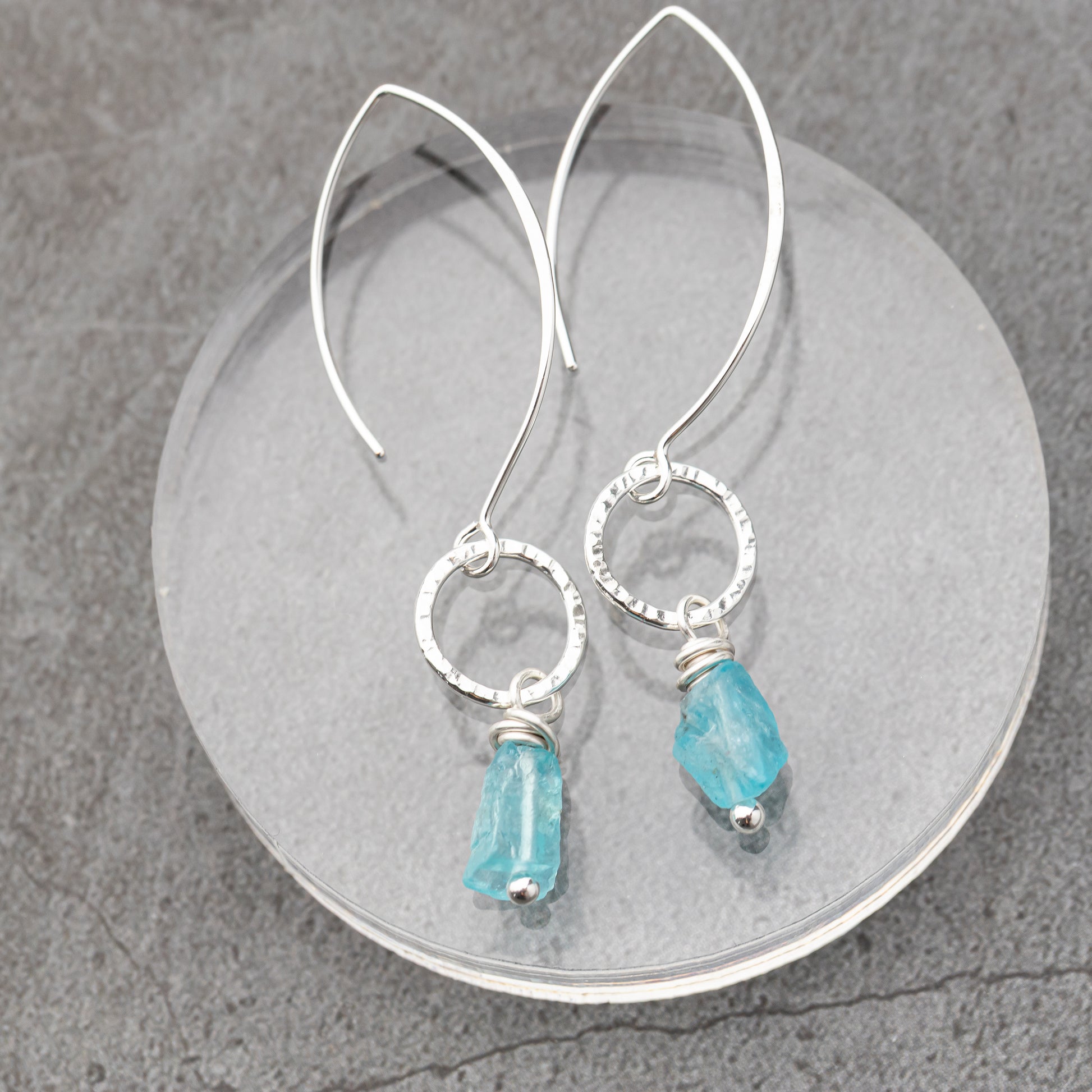 Silver earrings with blue apatite gemstones on a gray surface