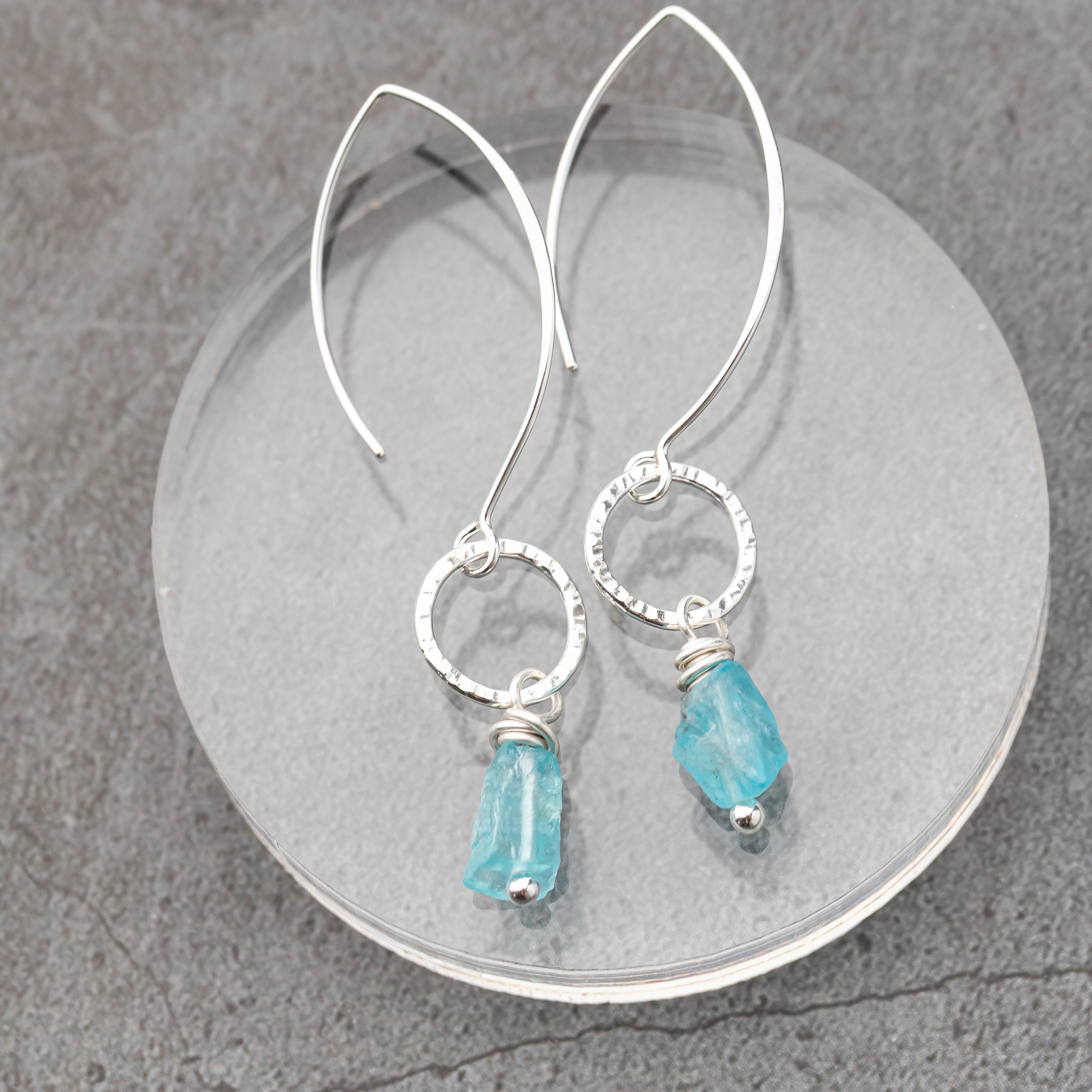 Silver earrings with blue apatite gemstones on a gray surface