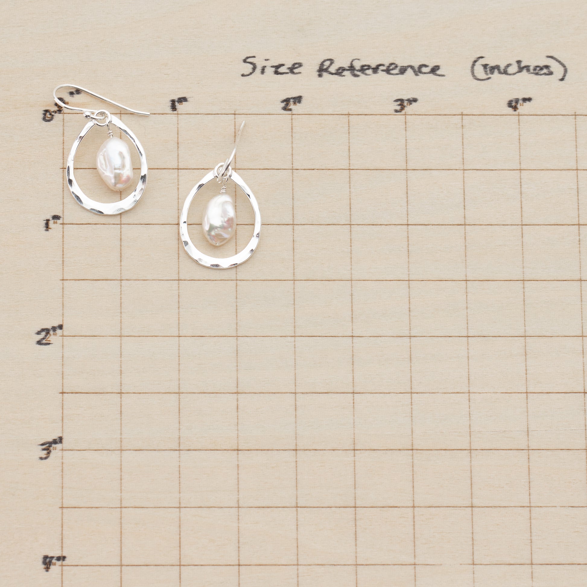 Pair of silver earrings with pearls on a size reference chart.