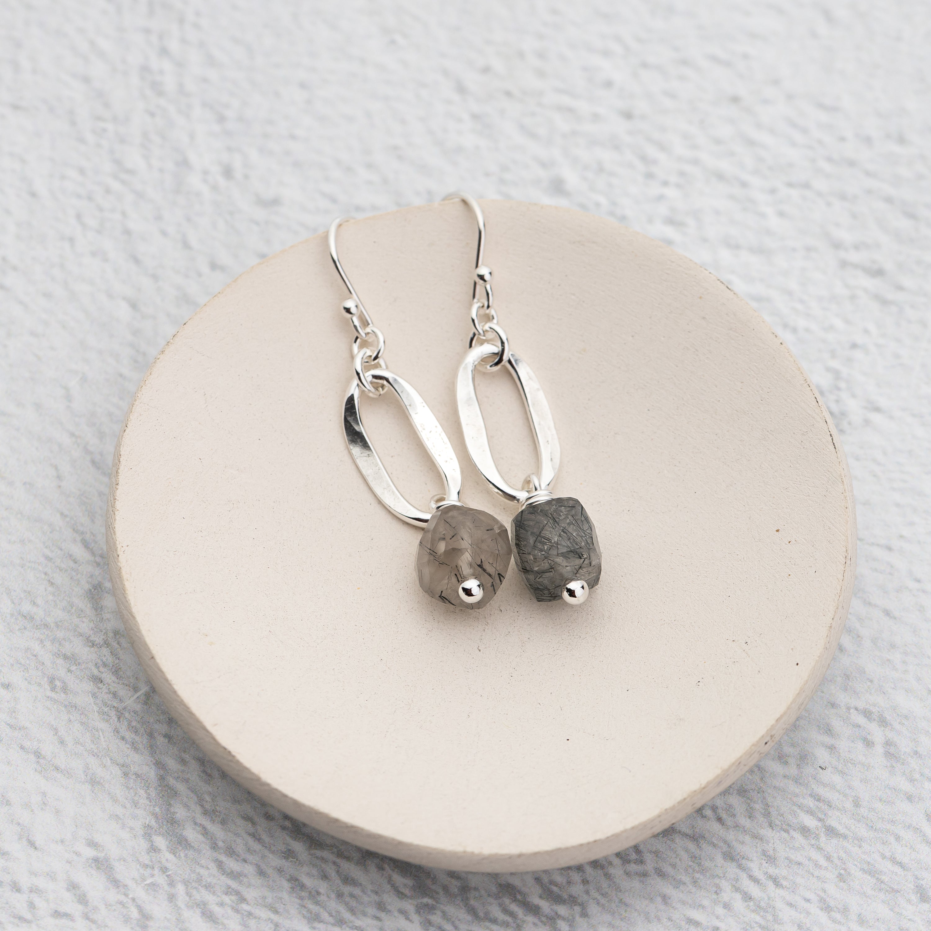 Silver earrings with stone cube beads on a round stone surface