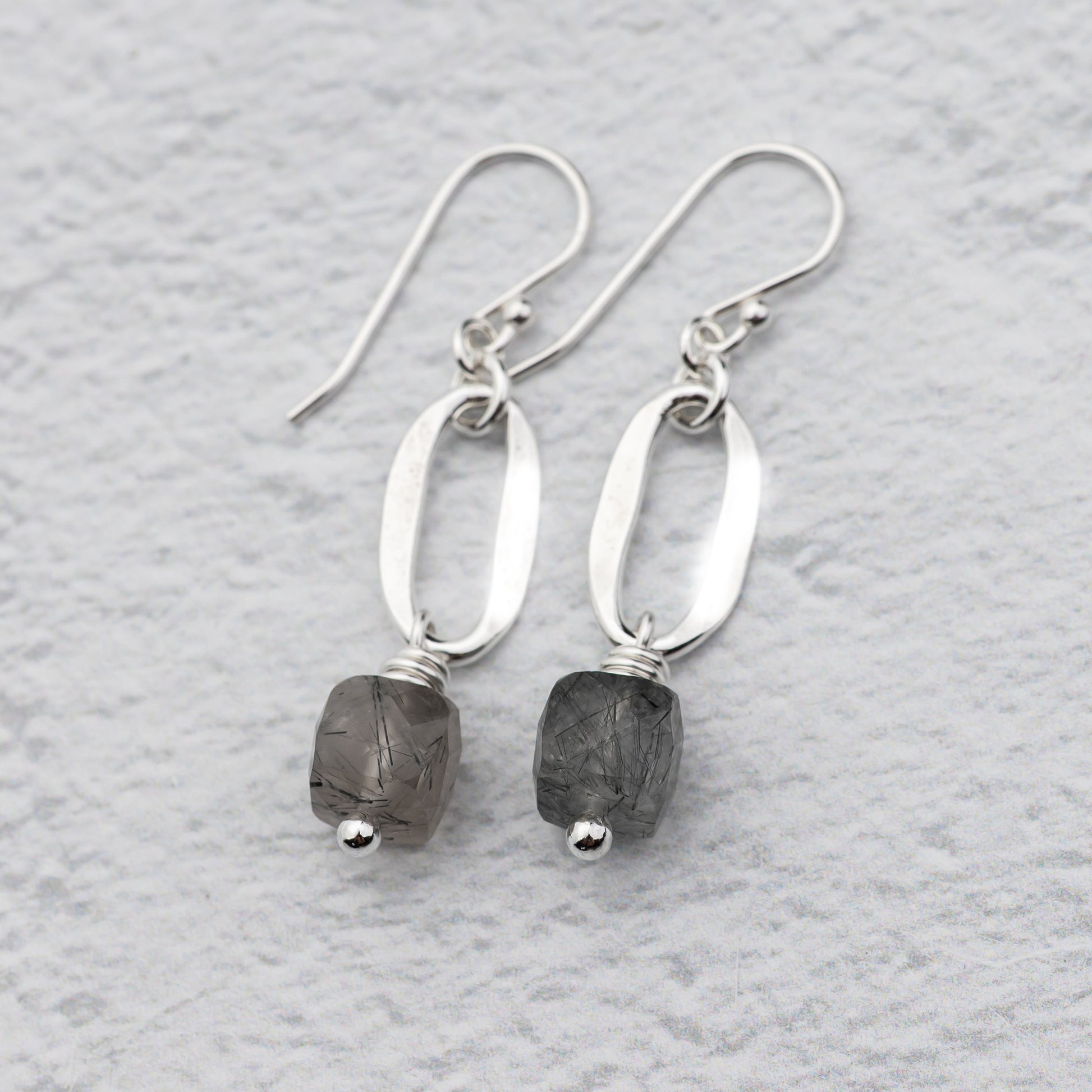 handmade sterling silver earrings with hammered silver ovals and tourmalinated quartz gemstones against a white background.