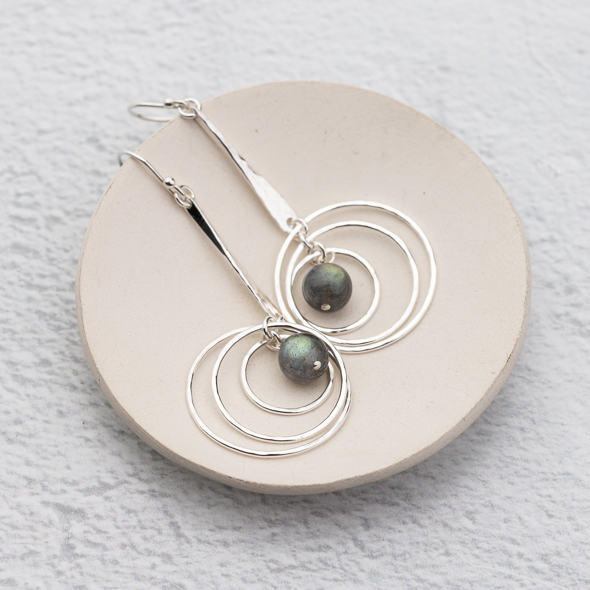 handmade and hammer textured silver labradorite earrings on a dish with orbiting circles
