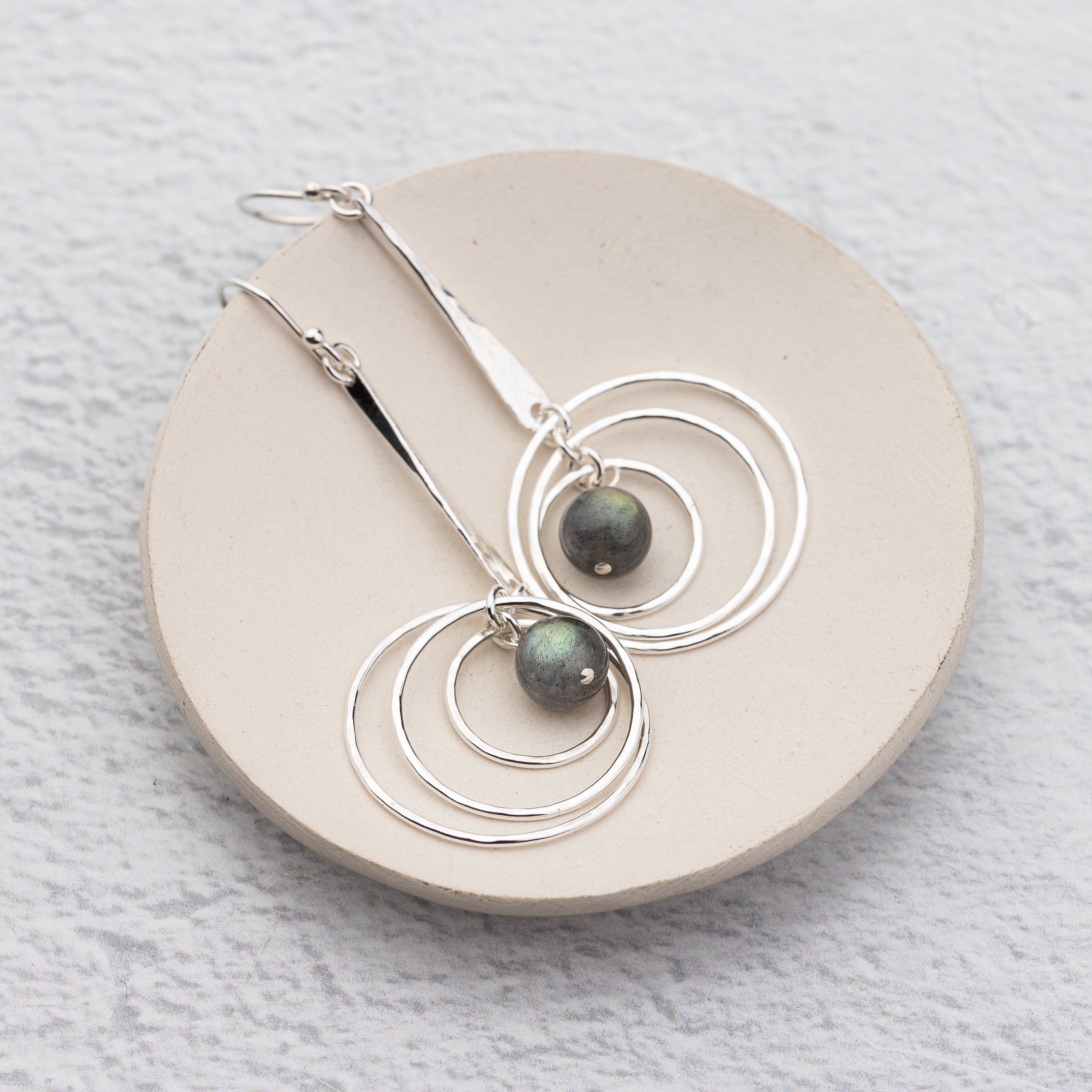 handmade and hammer textured silver labradorite earrings on a dish with orbiting circles
