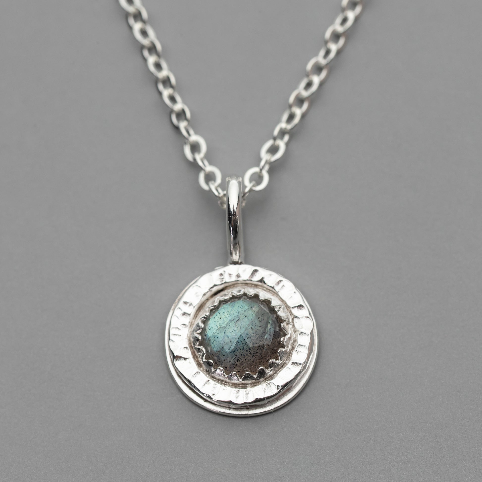 close up of a small round pendant, the pendant is handmade with sterling silver and has a rose cut labradorite gemstone with a blue green flash.
