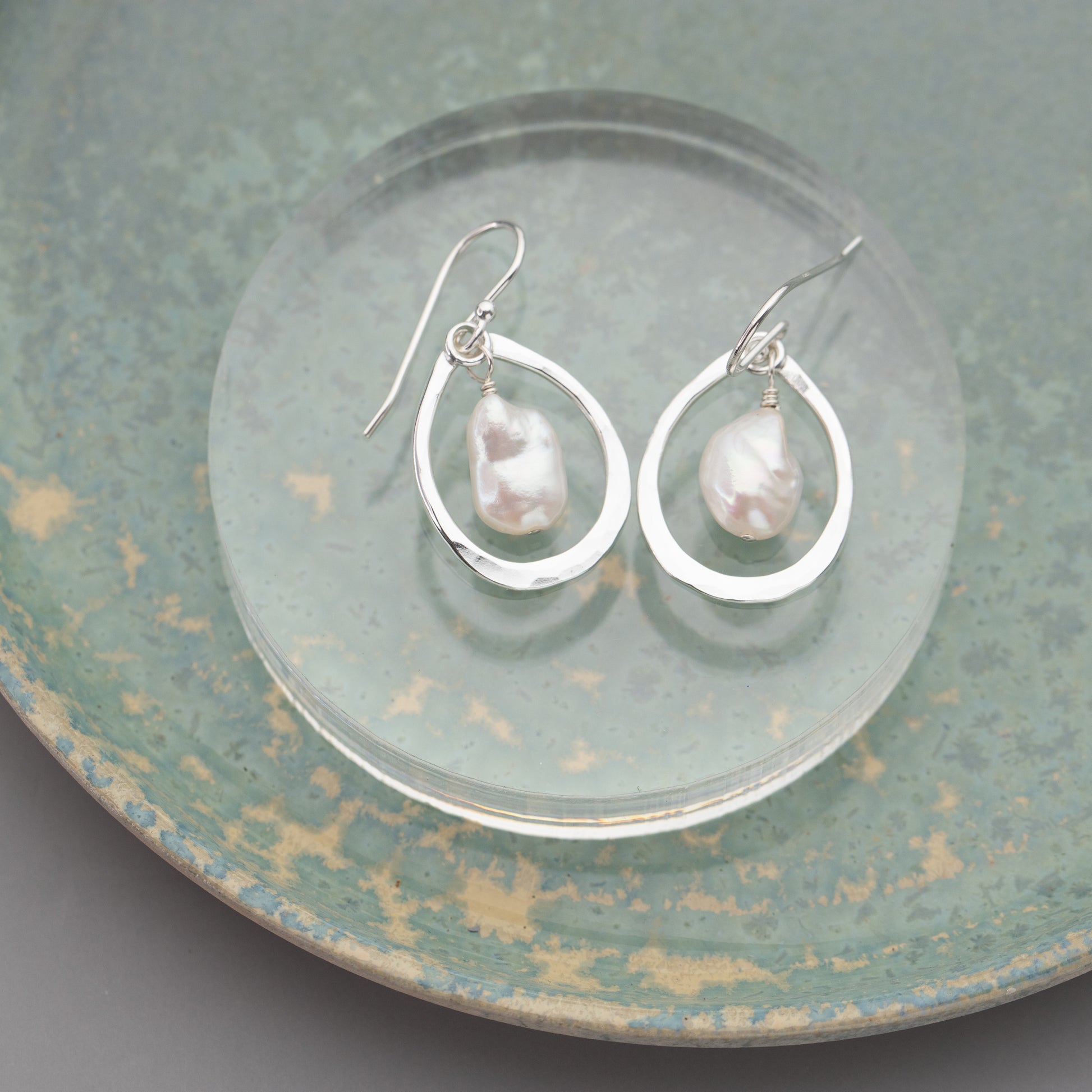 Silver silver handmade  teardrop earrings with pearl drops on a textured green plate