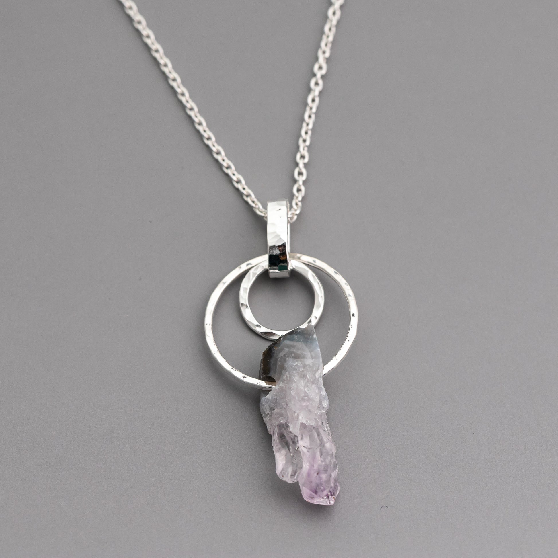 Handmade sterling silver necklace with a circle pendant and purple amethyst crystal on a gray background