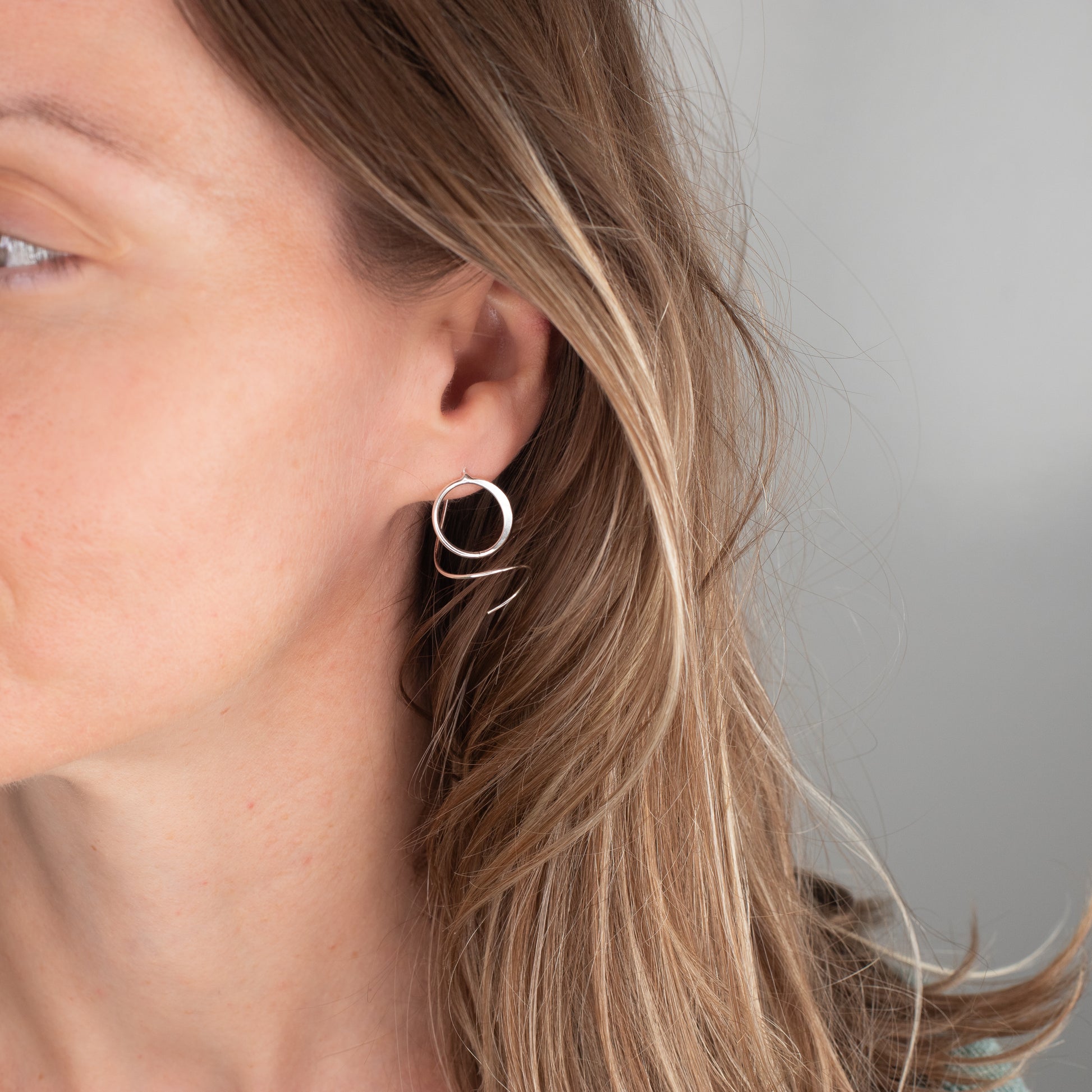 Close-up of a person wearing a silver spiral hoop earring with a neutral background