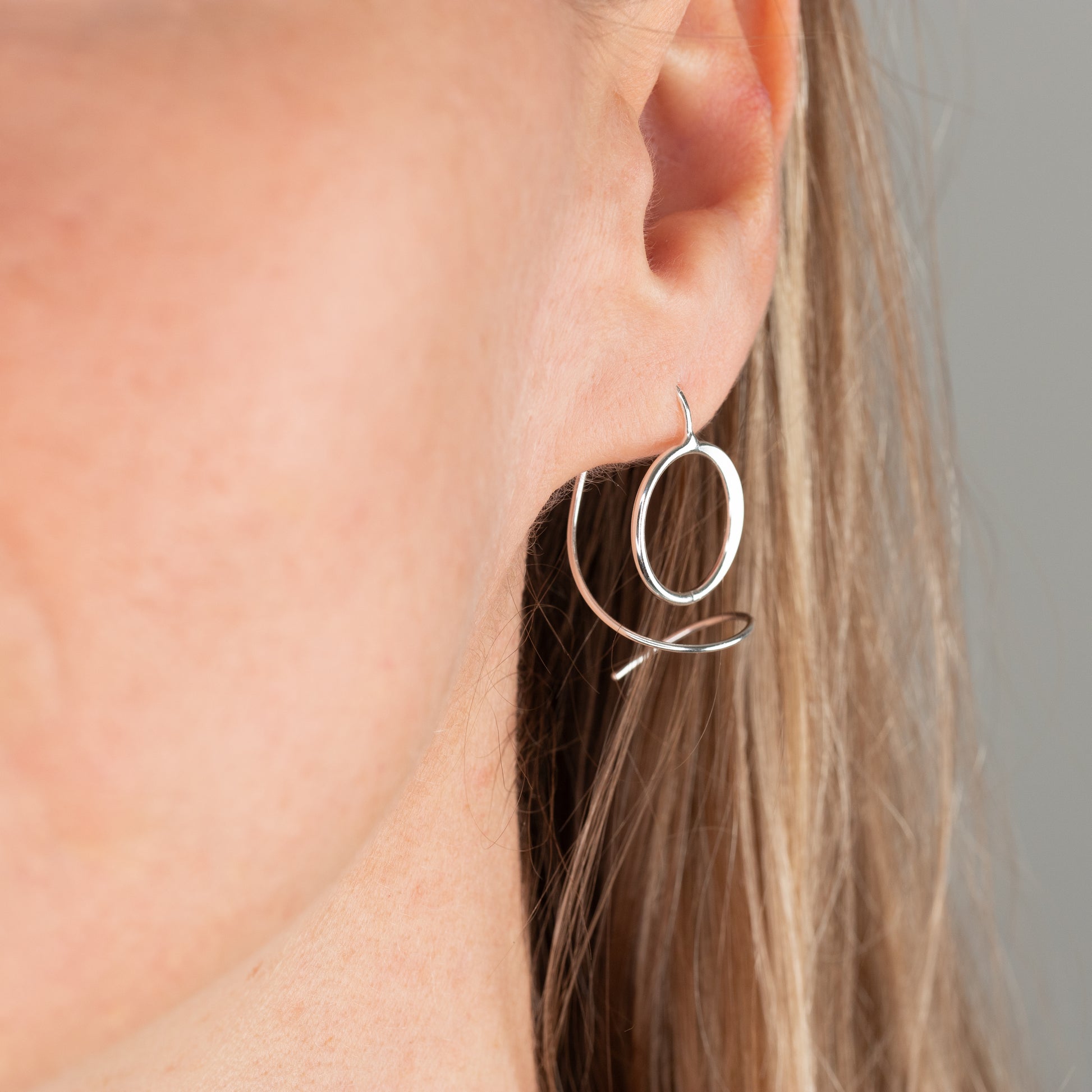 unique sterling Silver hoop earring worn by a person with a neutral background
