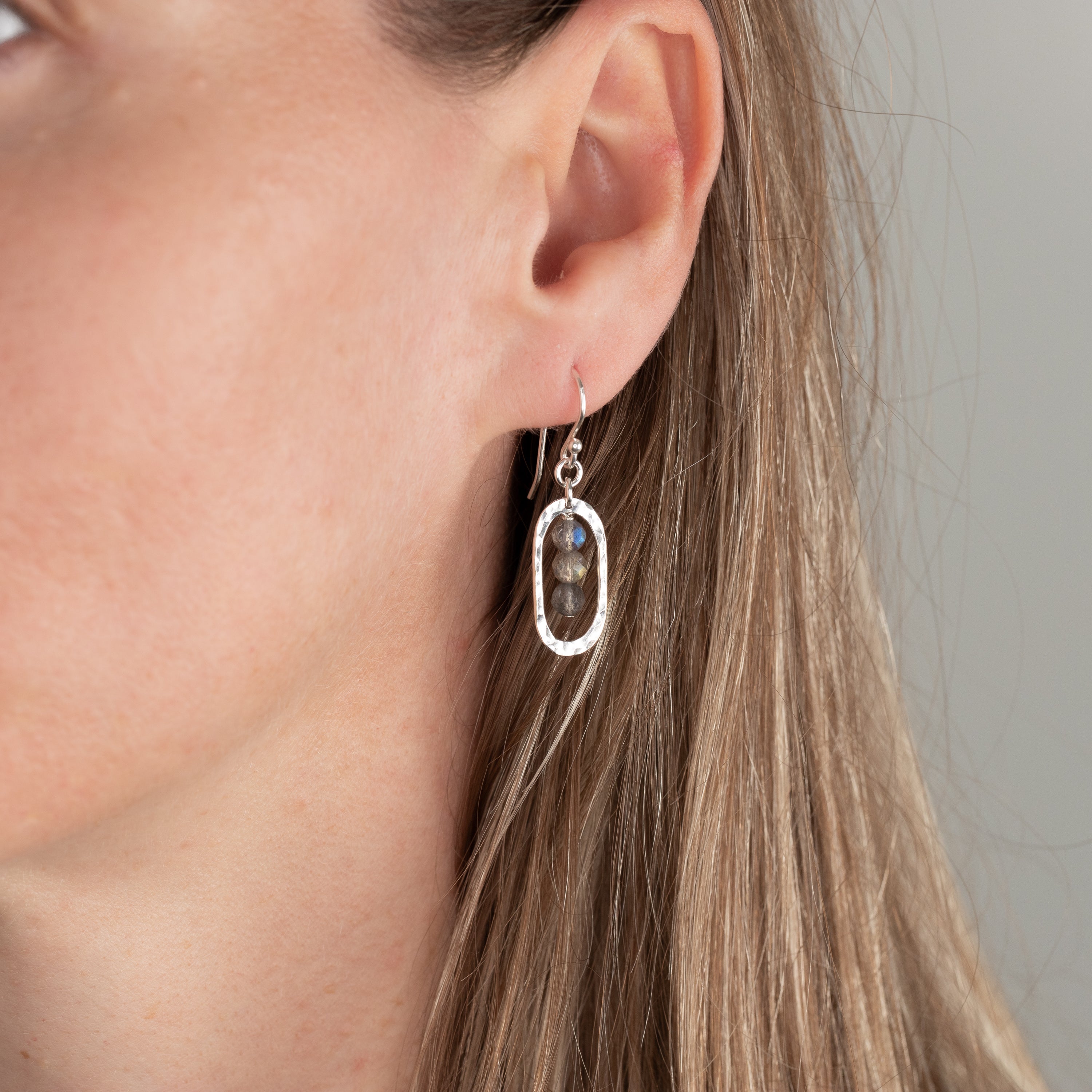 Close-up of a person wearing a silver earring with labradorite gemstones.