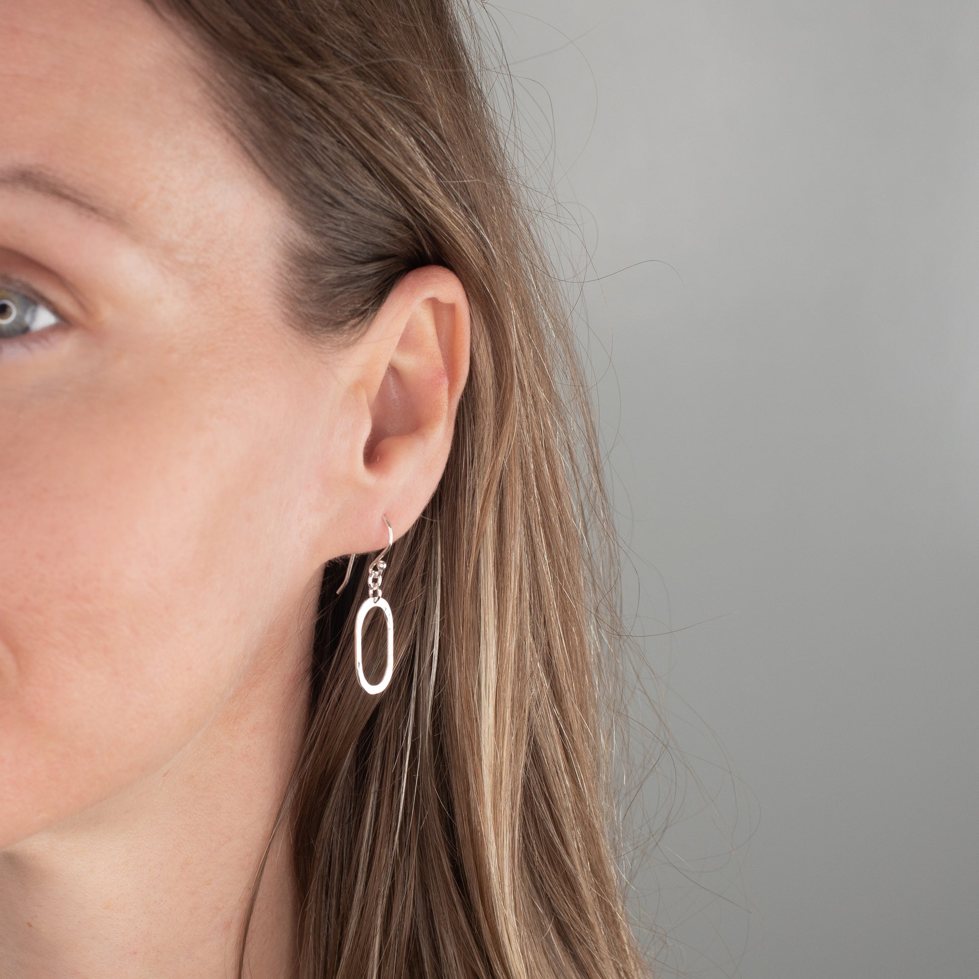 Close-up of a person wearing a hammered silver oval earring against a neutral background