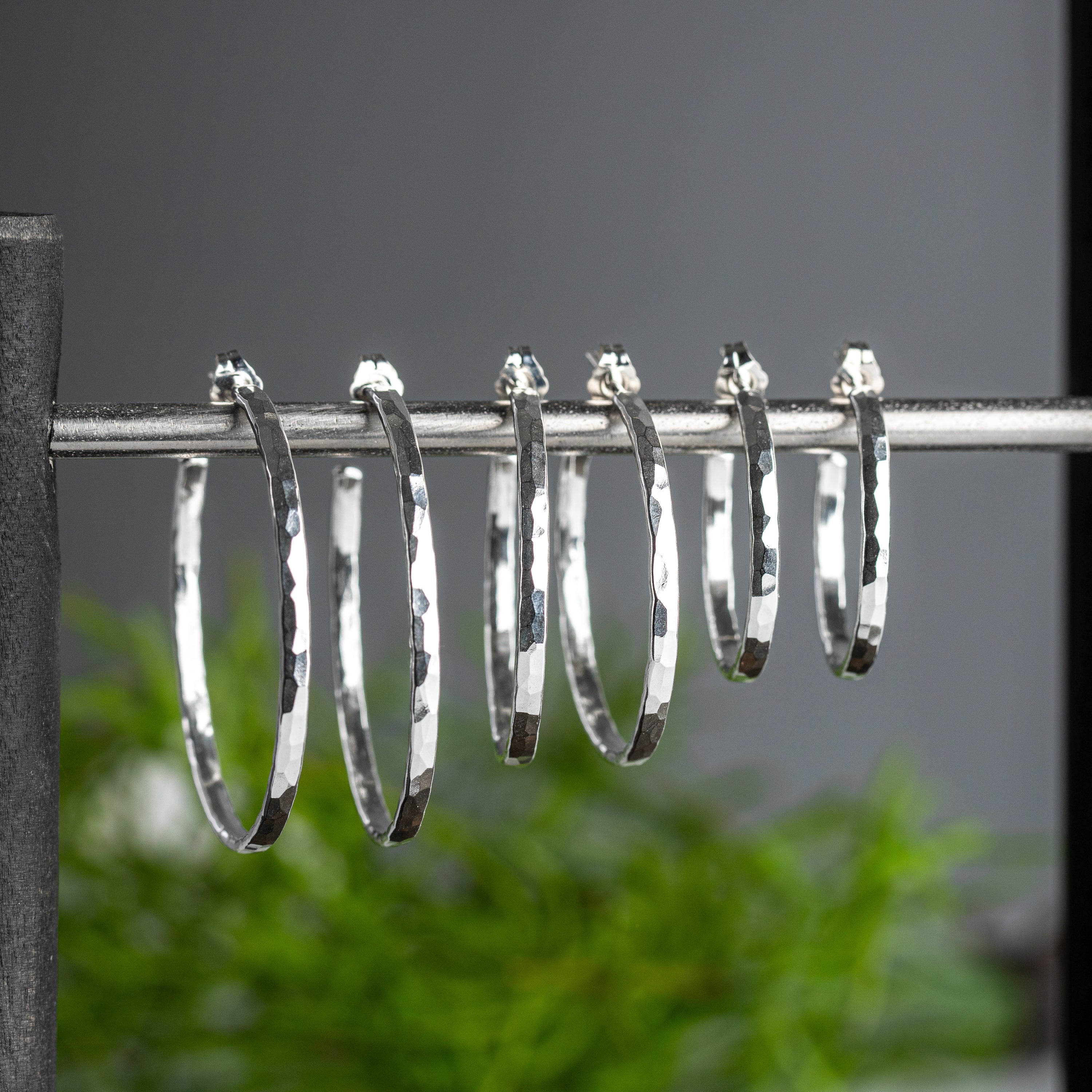 hand hammered sterling silver hoop earrings with a post are shown in three sizes hanging from a jewelry bar