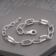 A handmade sterling silver link chain bracelet with elongated oval links and a lobster clasp, displayed on a gray textured surface. Through Thick and Thin Design