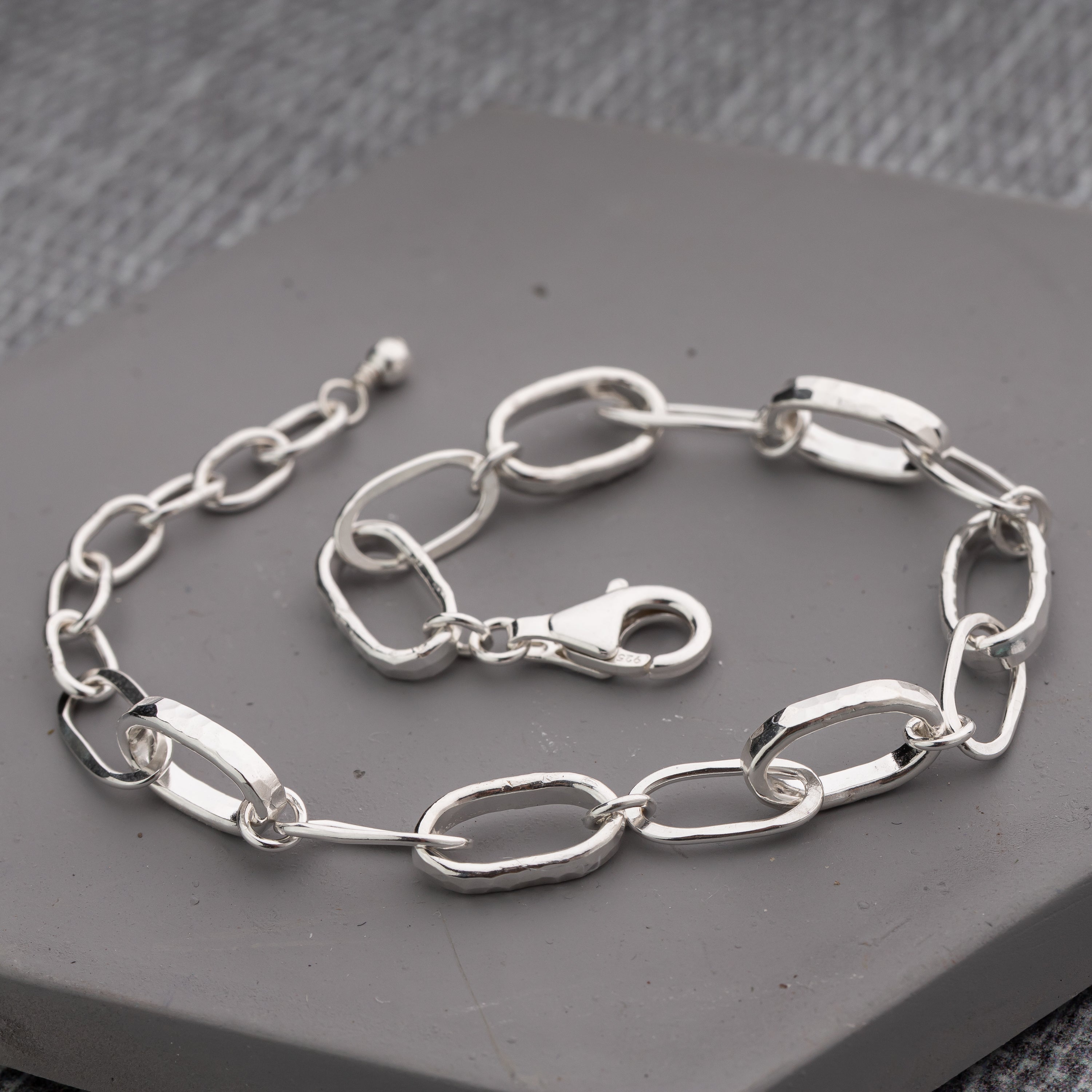 A handmade sterling silver link chain bracelet with elongated oval links and a lobster clasp, displayed on a gray textured surface. Through Thick and Thin Design